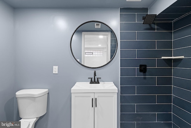 bathroom with toilet, tiled shower, and vanity