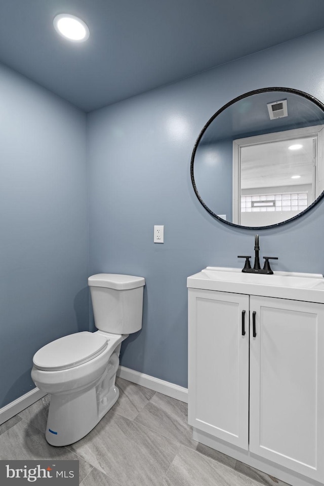 bathroom featuring toilet, vanity, baseboards, and visible vents