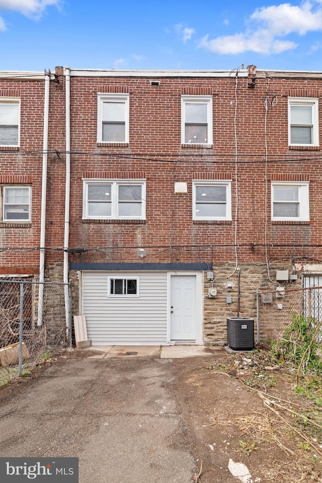 rear view of property with central AC unit, fence, and brick siding