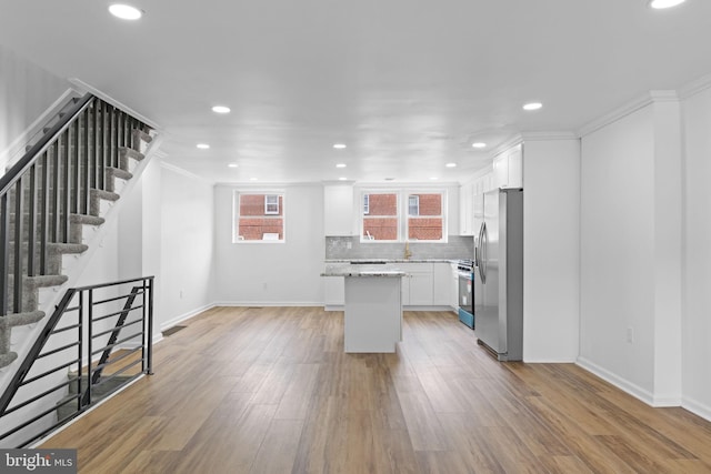 kitchen featuring gas range oven, light wood-type flooring, freestanding refrigerator, backsplash, and white cabinets