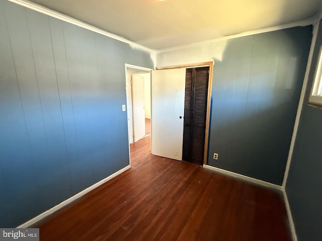 unfurnished bedroom featuring baseboards, dark wood finished floors, ornamental molding, and a closet