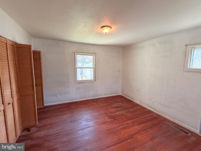 unfurnished bedroom featuring visible vents, multiple windows, and wood finished floors