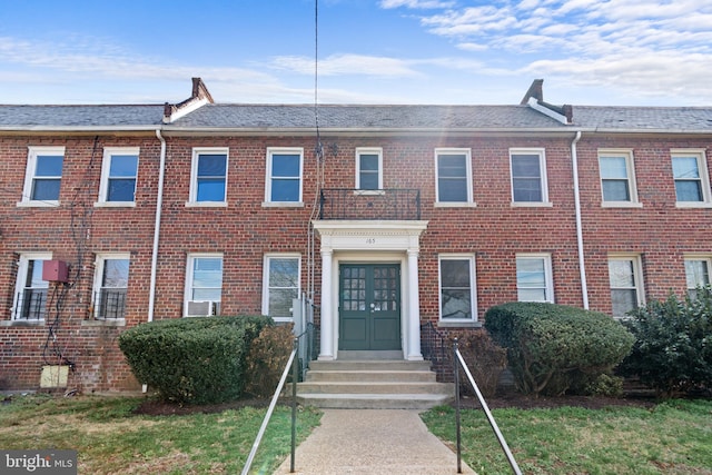 view of property with brick siding, entry steps, and roof with shingles
