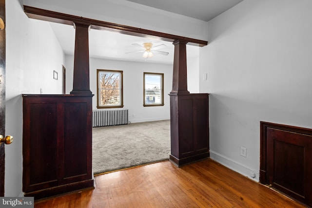 unfurnished living room featuring baseboards, a ceiling fan, radiator heating unit, decorative columns, and wood-type flooring