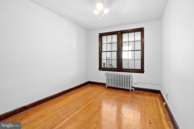 unfurnished room with wood-type flooring, radiator heating unit, a ceiling fan, and baseboards