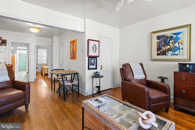 living area featuring ceiling fan, hardwood / wood-style flooring, and baseboards