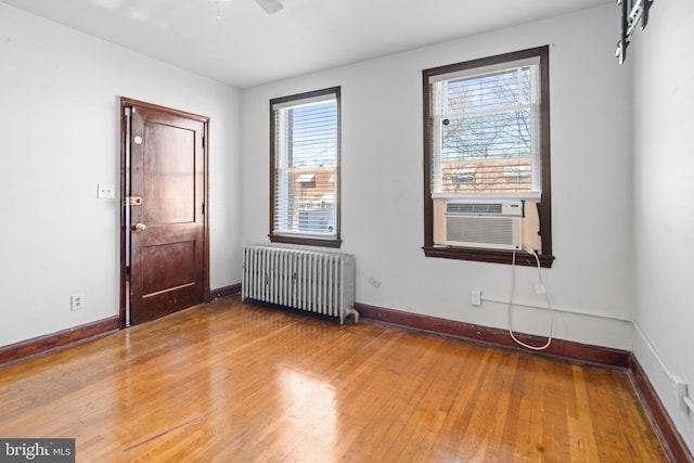spare room featuring radiator heating unit, ceiling fan, hardwood / wood-style floors, and baseboards