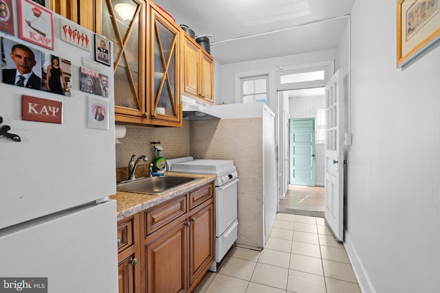 kitchen featuring light tile patterned floors, a sink, white appliances, under cabinet range hood, and brown cabinetry