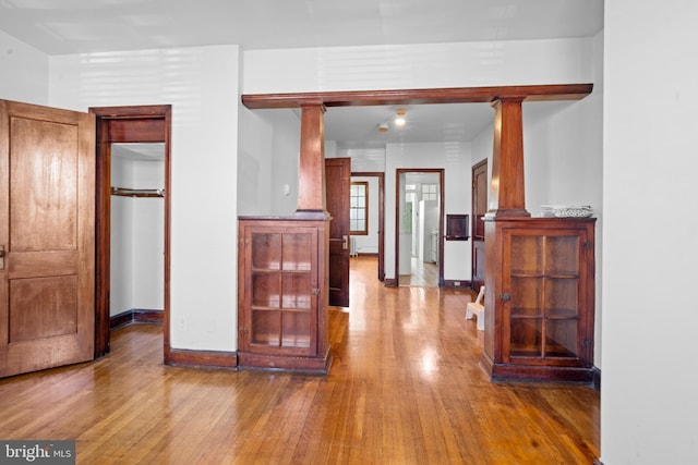 hall featuring hardwood / wood-style floors, baseboards, and ornate columns