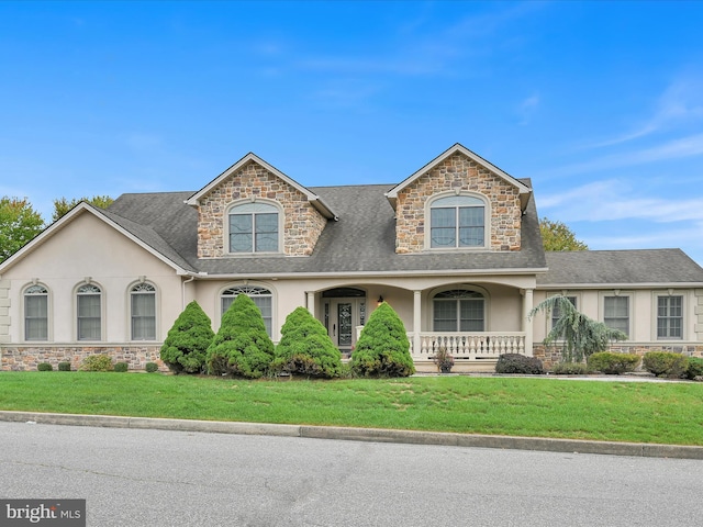 view of front facade featuring covered porch, stucco siding, stone siding, and a front yard