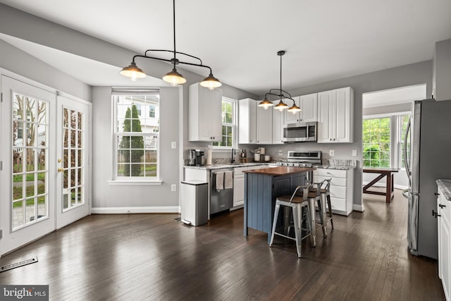 kitchen with appliances with stainless steel finishes, a center island, white cabinetry, a wealth of natural light, and visible vents