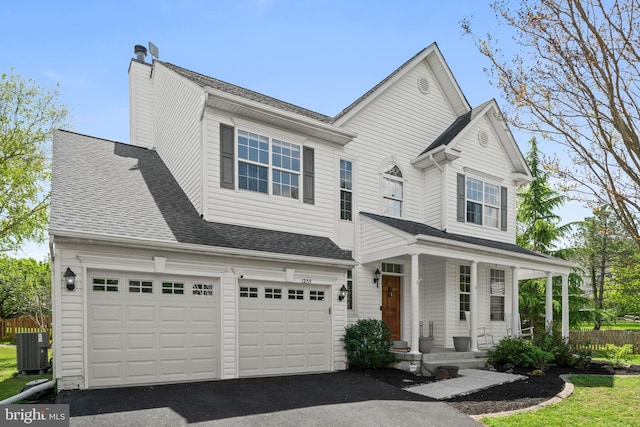 traditional home with an attached garage, central AC, aphalt driveway, a chimney, and covered porch