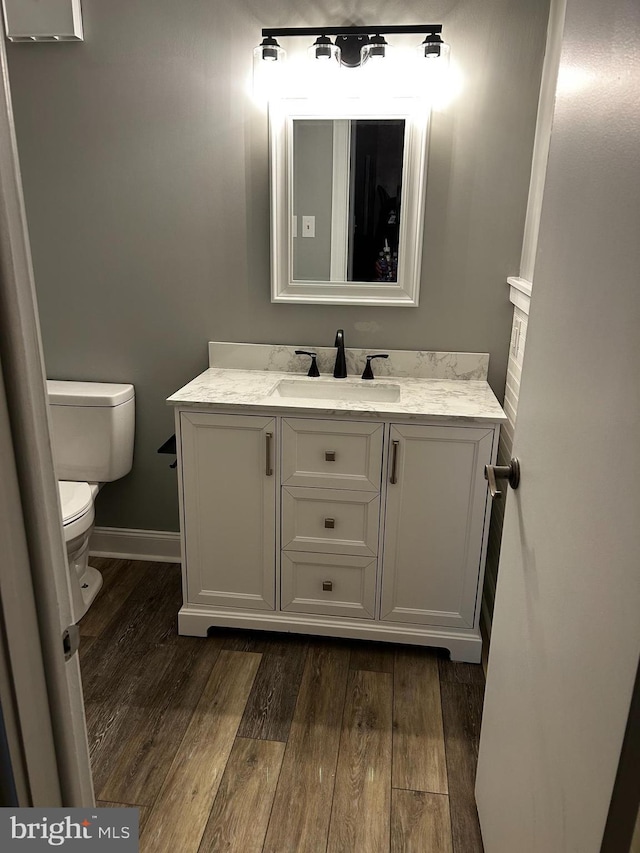 half bathroom with vanity, baseboards, toilet, and wood finished floors