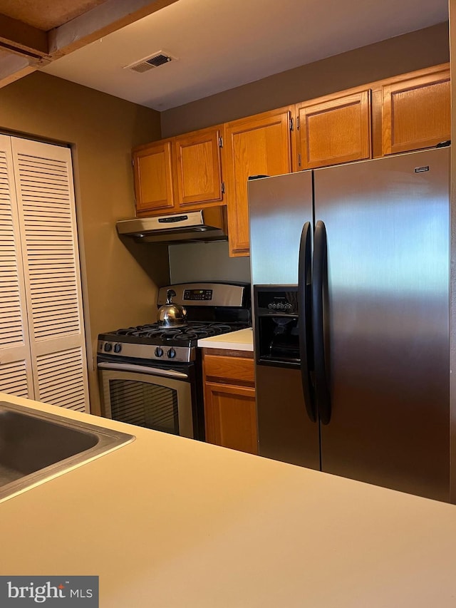 kitchen featuring light countertops, under cabinet range hood, visible vents, stainless steel appliances, and a sink