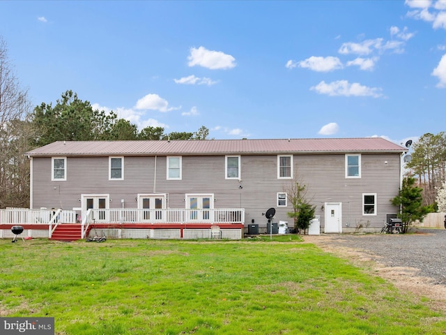 back of property featuring metal roof, a wooden deck, and a lawn