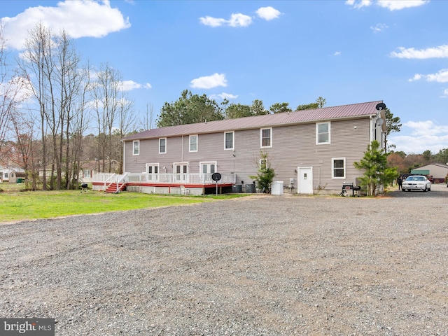 back of property featuring a wooden deck, metal roof, and a lawn