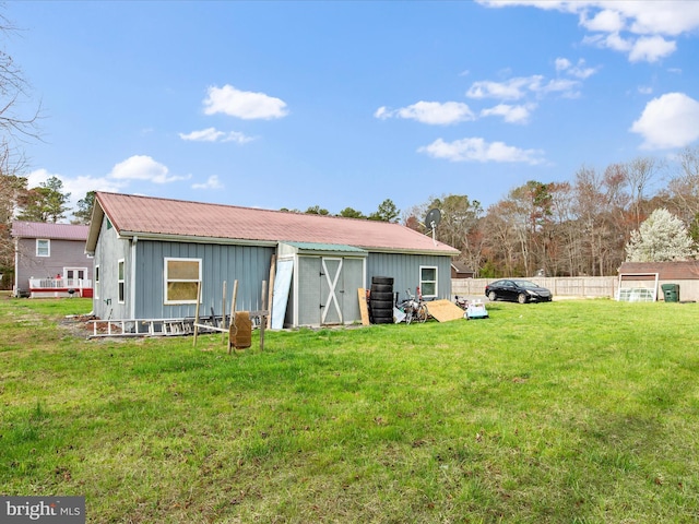 back of property with a lawn, board and batten siding, fence, a storage unit, and an outbuilding