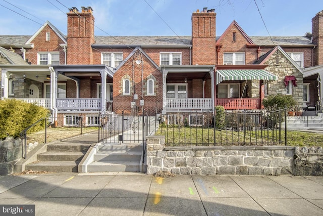 multi unit property with brick siding, covered porch, a fenced front yard, and a chimney