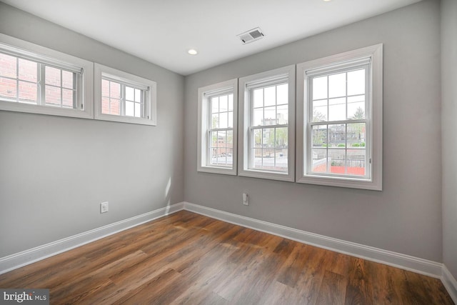 spare room with plenty of natural light, dark wood-type flooring, visible vents, and baseboards