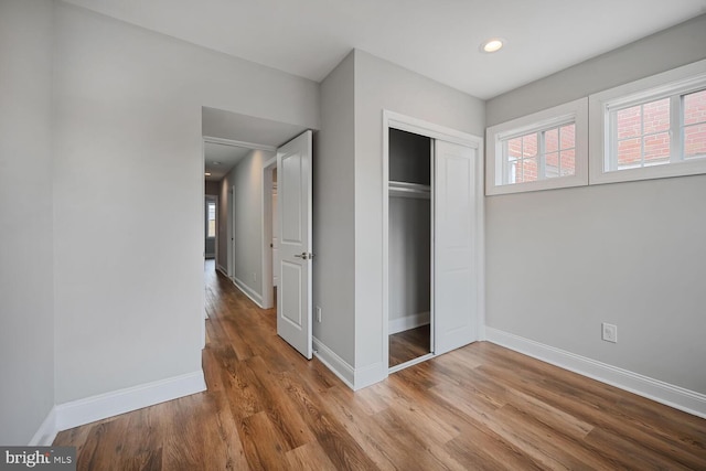 unfurnished bedroom featuring wood finished floors, baseboards, a closet, and recessed lighting