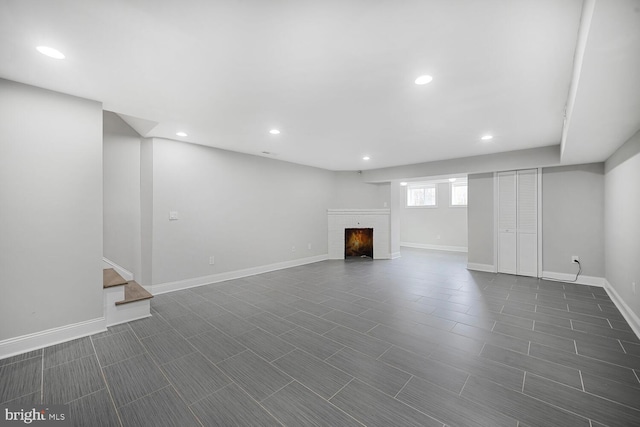 basement featuring a warm lit fireplace, baseboards, recessed lighting, and stairs