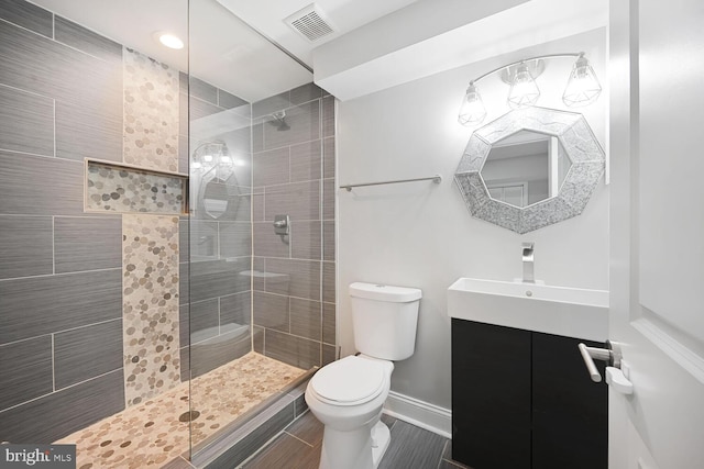 bathroom with tiled shower, vanity, visible vents, toilet, and baseboards