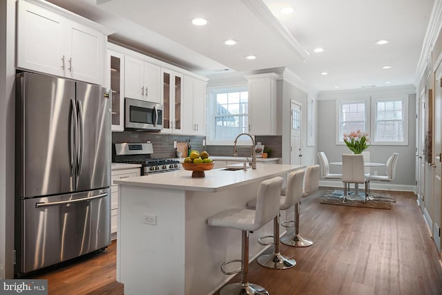 kitchen featuring tasteful backsplash, ornamental molding, white cabinets, appliances with stainless steel finishes, and a sink