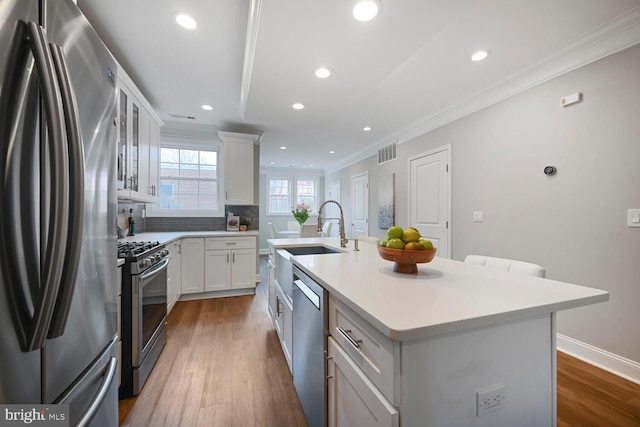 kitchen featuring crown molding, wood finished floors, a kitchen island with sink, a sink, and stainless steel appliances