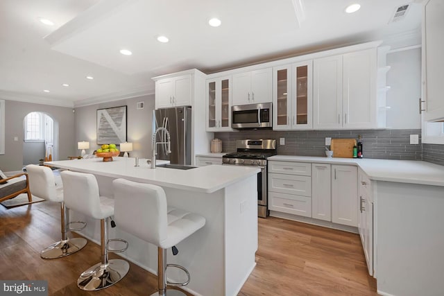 kitchen featuring crown molding, appliances with stainless steel finishes, a center island with sink, and light wood finished floors