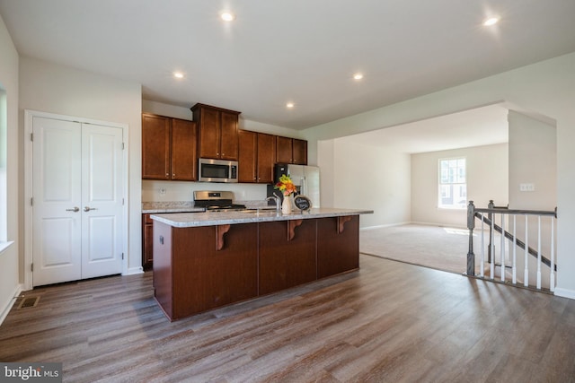 kitchen with stainless steel appliances, an island with sink, a kitchen breakfast bar, and wood finished floors