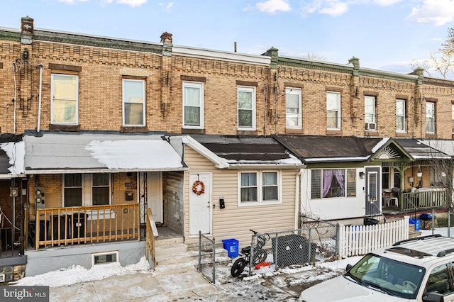 view of property featuring brick siding, a porch, and fence