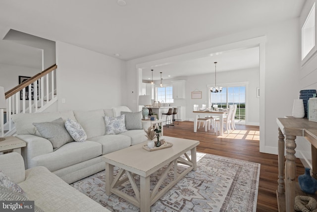 living area featuring stairs, a notable chandelier, baseboards, and wood finished floors