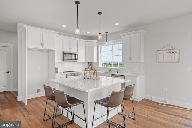 kitchen featuring a breakfast bar, stainless steel appliances, white cabinets, visible vents, and baseboards