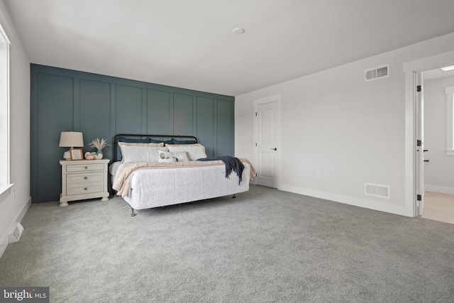 carpeted bedroom featuring a decorative wall, baseboards, and visible vents