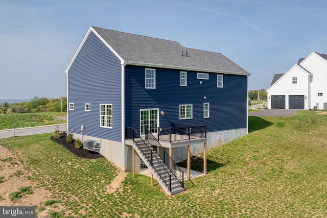 back of property with a yard, a garage, stairs, a deck, and roof with shingles