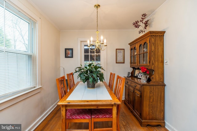 dining space with wood finished floors, crown molding, baseboards, and an inviting chandelier