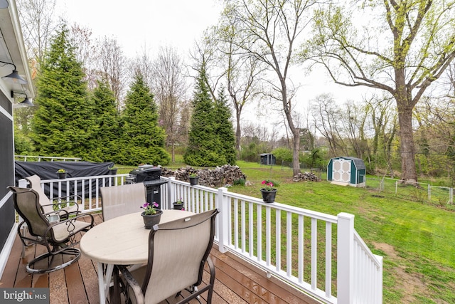 wooden terrace featuring an outbuilding, a fenced backyard, a lawn, outdoor dining space, and a shed