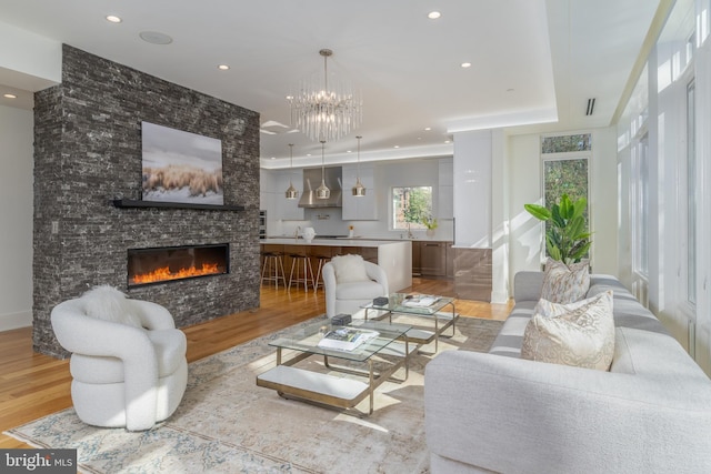 living room featuring a tray ceiling, a stone fireplace, light wood finished floors, and recessed lighting