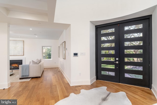 entrance foyer featuring baseboards, recessed lighting, french doors, light wood-style flooring, and a glass covered fireplace