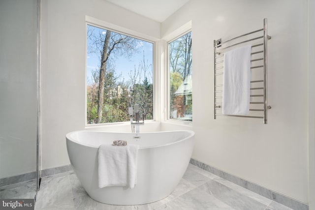 full bath with a soaking tub, marble finish floor, and baseboards