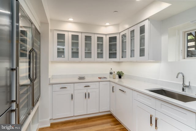 kitchen with a sink, light countertops, high quality fridge, light wood-style floors, and white cabinetry