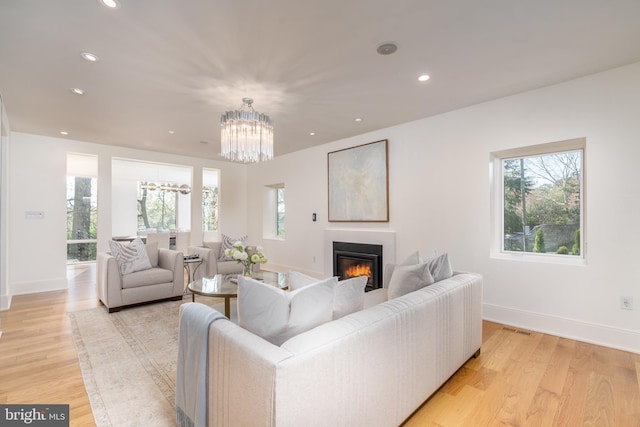 living room with a glass covered fireplace, recessed lighting, light wood-style floors, and an inviting chandelier