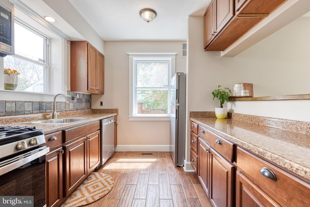 kitchen featuring brown cabinetry, baseboards, a sink, and appliances with stainless steel finishes