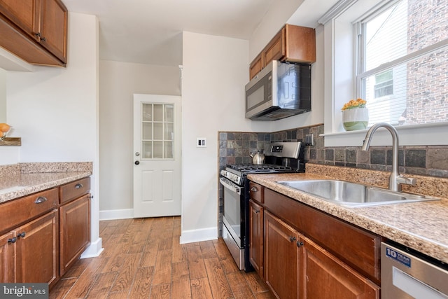 kitchen with a sink, brown cabinetry, light countertops, dark wood finished floors, and appliances with stainless steel finishes
