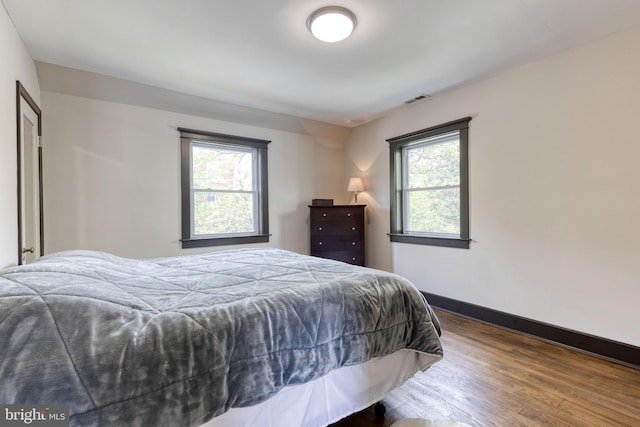 bedroom featuring baseboards, multiple windows, wood finished floors, and visible vents