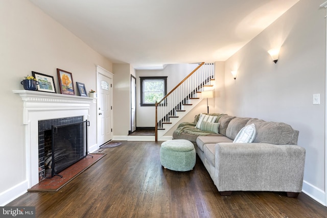 living room featuring dark wood-type flooring, stairway, a fireplace with raised hearth, and baseboards