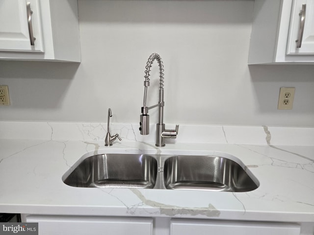 room details with a sink, white cabinets, and light stone counters