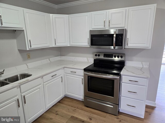 kitchen with crown molding, white cabinetry, a sink, stainless steel appliances, and light wood finished floors