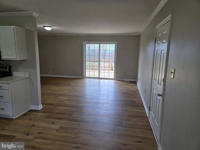unfurnished dining area with dark wood-type flooring, crown molding, and baseboards