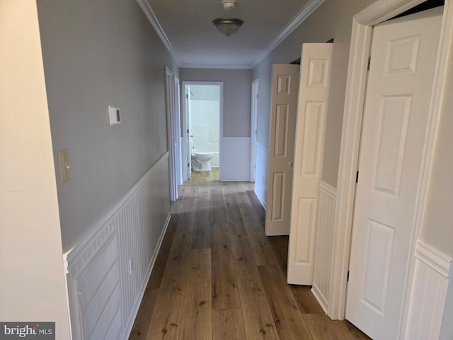 corridor featuring a decorative wall, wood-type flooring, a wainscoted wall, and crown molding